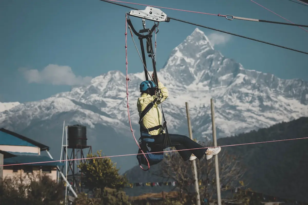 Person zip-lining over a green valley with mountains in the background
